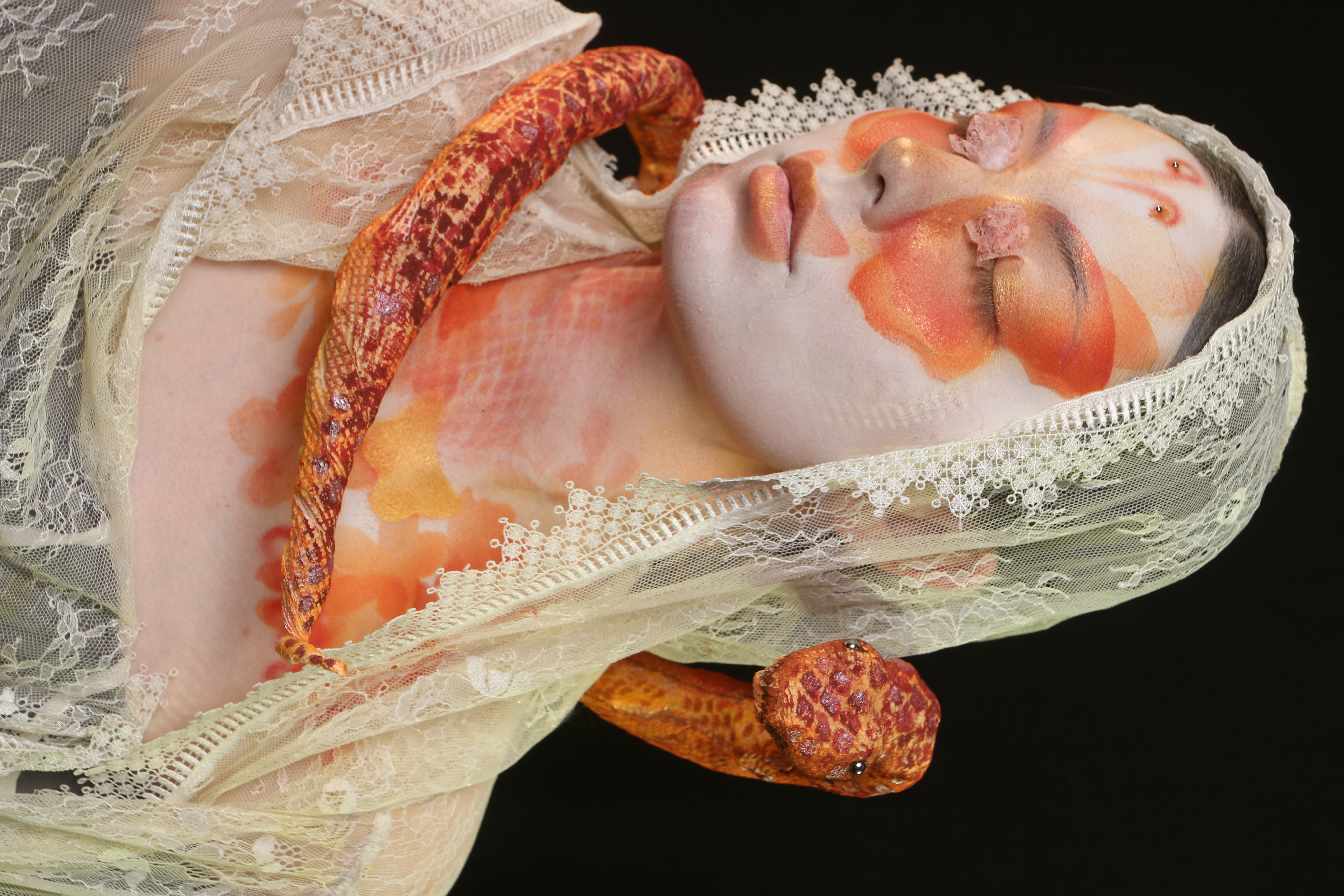 Front portrait of Lepidophis with butterfly-wing face makeup, lace details around the eyes, and an orange serpent behind the model.