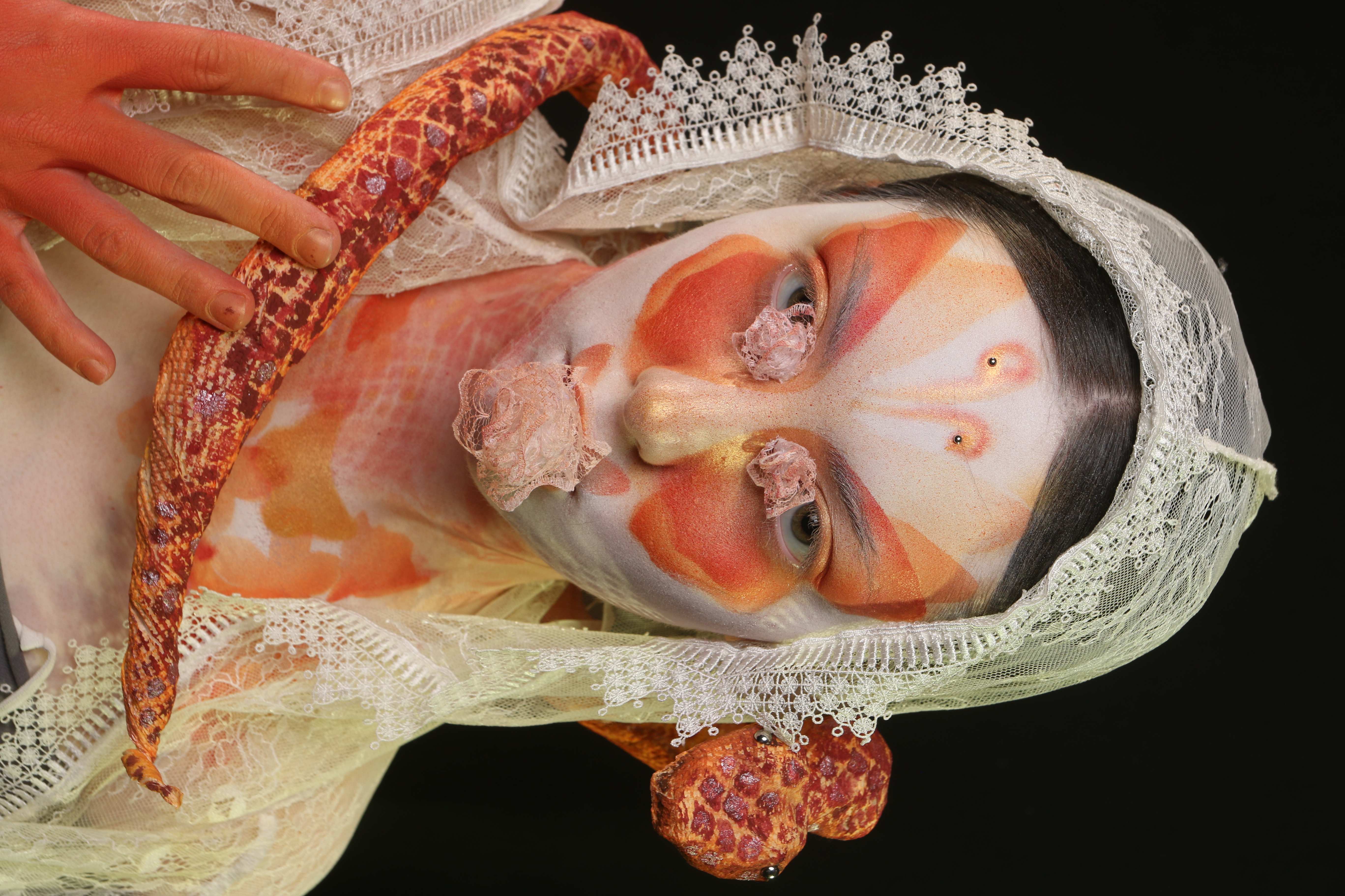 Close-up of Lepidophis featuring orange butterfly makeup, forehead embellishments, and a serpent coiled around the model’s neck.