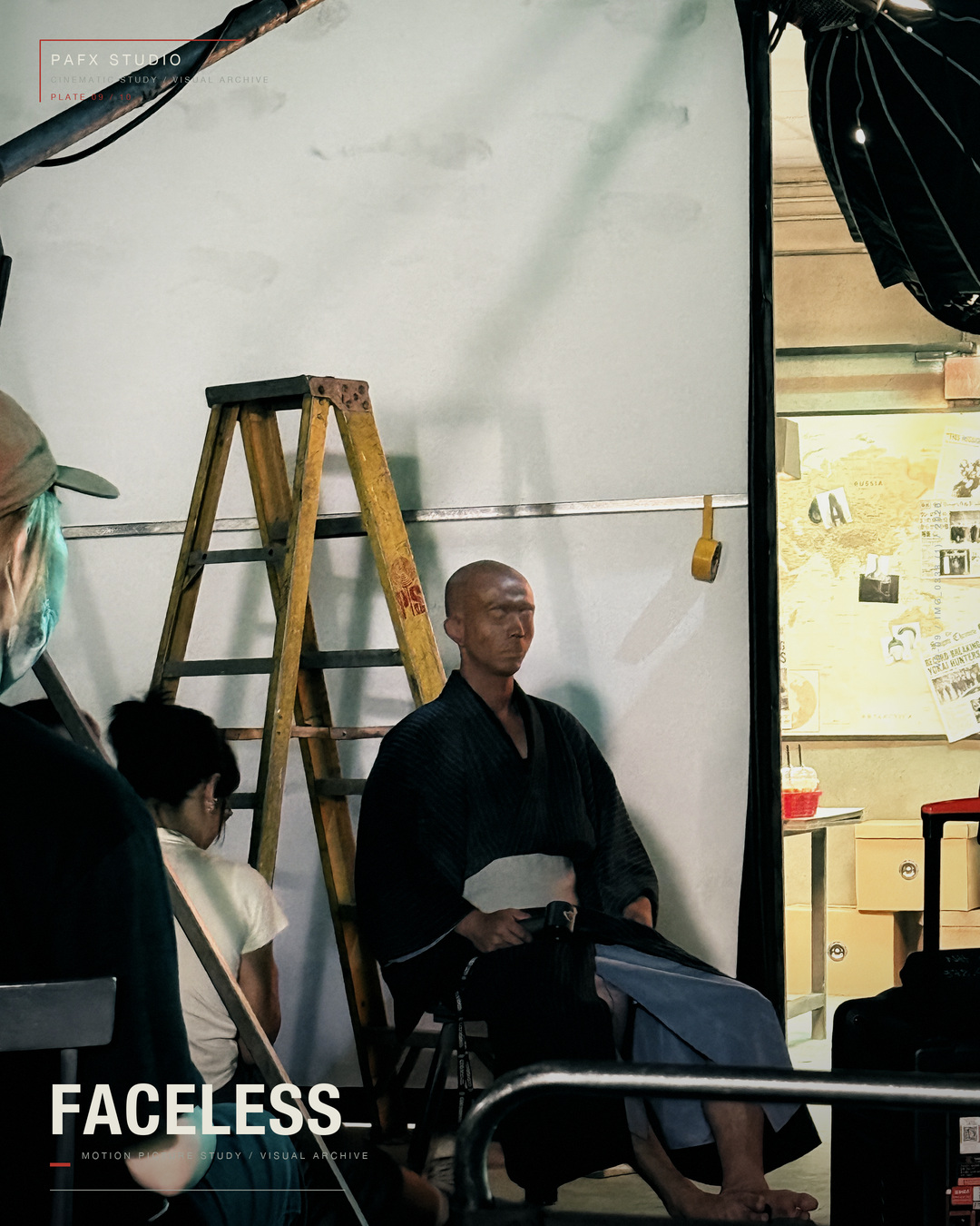 Wide behind-the-scenes view of the FACELESS character seated on set with production equipment visible.