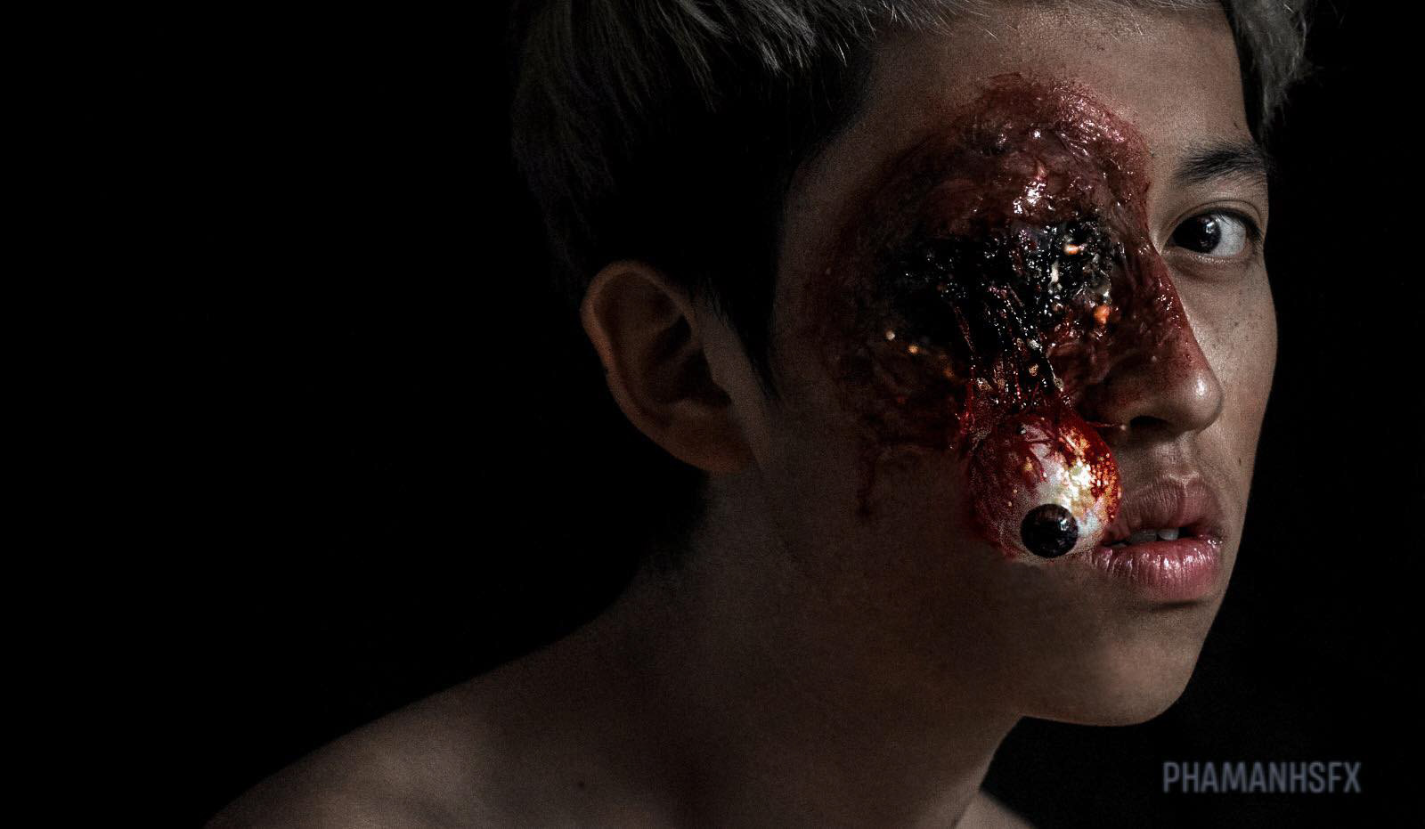 Close-up portrait of a performer wearing a silicone special effects makeup depicting a severe simulated injury around the eye.